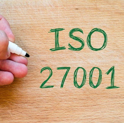 ISO 27001 is met een groene stift door iemand op een houten ondergrond geschreven