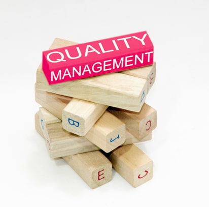 Wooden blocks, one of which is pink and has 'quality management' written on it