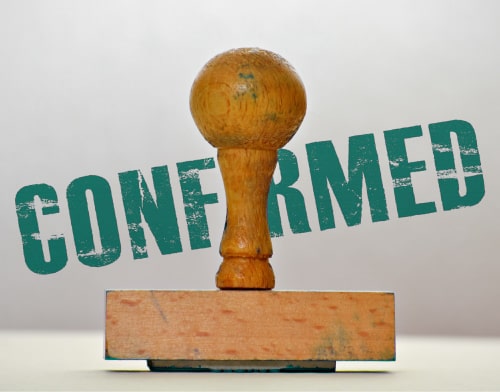 A close-up of a wooden stamp with the word 'confirmed' in the background