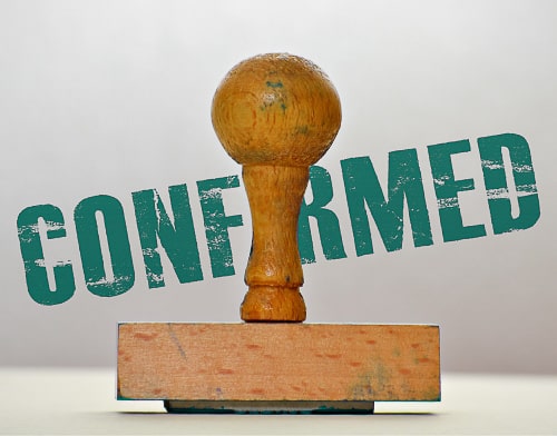 A close-up of a wooden stamp with the word 'confirmed' in the background