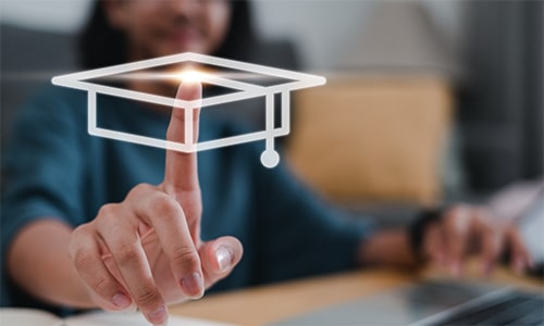 A person touches a digital image of a graduation cap on a screen, symbolising online learning or education.